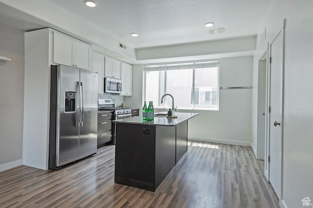 5306 W Solafax Ln, Herriman, UT 84096 - kitchen with stainless steel appliances, wood finished floors, white cabinets, a kitchen island with sink, and dark stone countertops