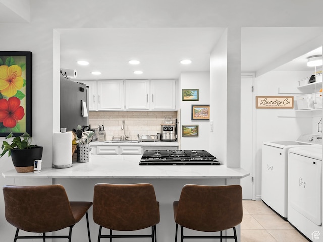5423 S Tonalea Dr, Murray, UT 84107 - kitchen featuring washing machine and dryer, a peninsula, white cabinetry, a kitchen breakfast bar, and tasteful backsplash