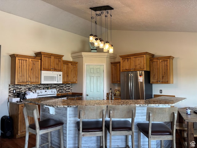 2673 S 2400 W, Weston, ID 83286 - kitchen featuring freestanding refrigerator, white microwave, brown cabinetry, decorative backsplash, and vaulted ceiling