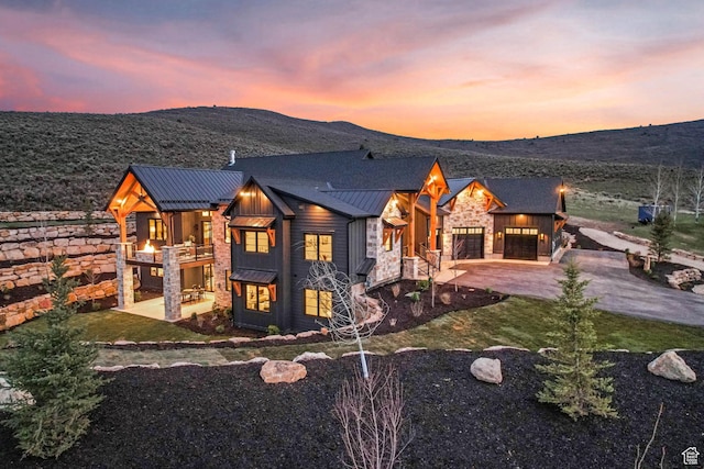 2225 Elk Meadows Cir, Woodland, UT 84036 - back of property at dusk featuring a standing seam roof, stone siding, an attached garage, board and batten siding, and driveway