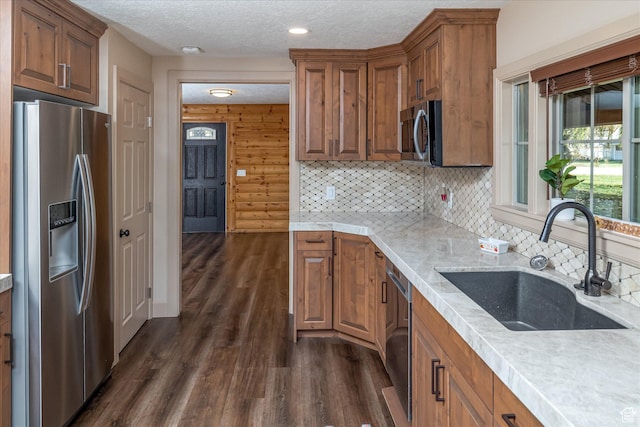 210 S 100 E, Fielding, UT 84311 - kitchen with appliances with stainless steel finishes, dark wood-style flooring, brown cabinets, a textured ceiling, and decorative backsplash