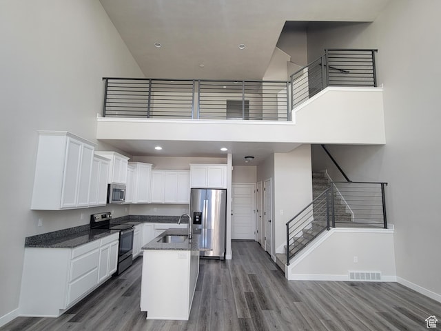 15040 S Wild Horse Way, Bluffdale, UT 84065 - kitchen featuring appliances with stainless steel finishes, a towering ceiling, white cabinetry, wood finished floors, and dark stone countertops