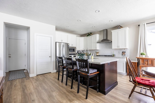 1681 S 1110 E, Heber City, UT 84032 - kitchen featuring wall chimney exhaust hood, appliances with stainless steel finishes, light wood-style flooring, a kitchen bar, and a textured ceiling