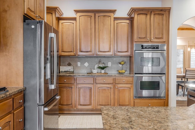 10677 S Amberley Ln E, Sandy, UT 84094 - kitchen with stainless steel appliances, arched walkways, tasteful backsplash, light stone countertops, and brown cabinets