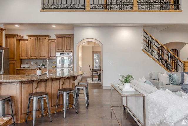 10677 S Amberley Ln E, Sandy, UT 84094 - kitchen with arched walkways, stainless steel appliances, a breakfast bar area, light stone counters, and recessed lighting