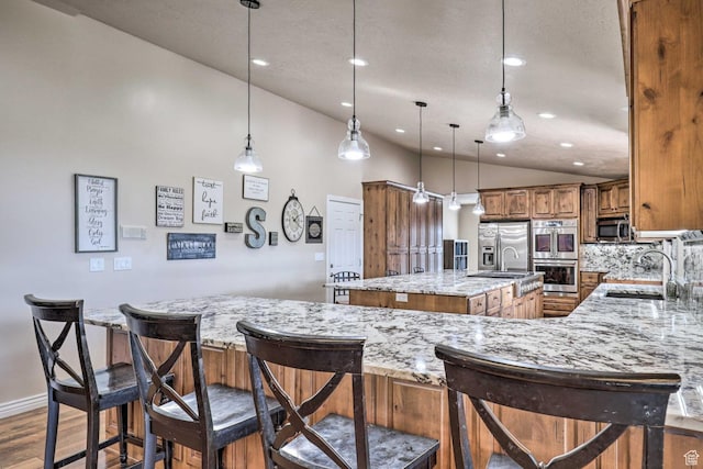 3572 Wild Mare Way, Heber City, UT 84032 - kitchen with a center island with sink, brown cabinets, appliances with stainless steel finishes, wood finished floors, and light stone countertops