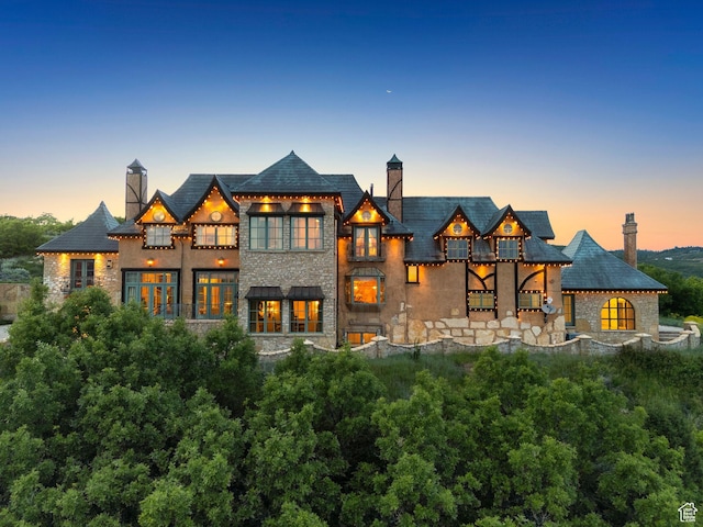 1526 W Red Hawk Trl, Park City, UT 84098 - back of house at dusk featuring a balcony, stone siding, a chimney, stucco siding, and a high end roof