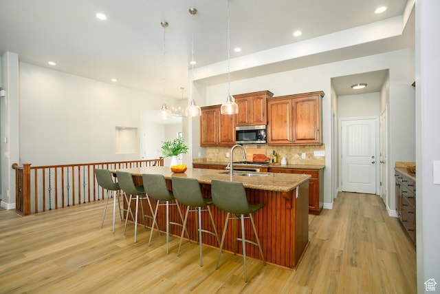 1103 Vista Dr, Santaquin, UT 84655 - kitchen featuring stainless steel microwave, light wood finished floors, a breakfast bar, an island with sink, and brown cabinetry