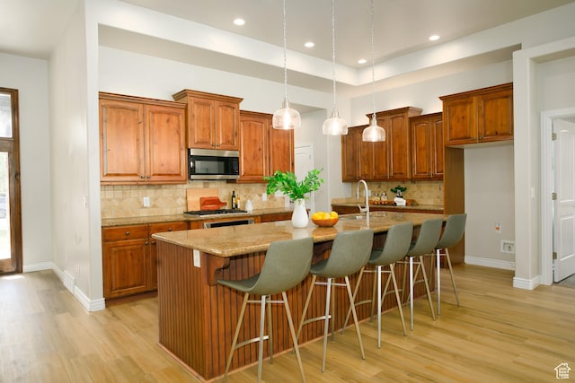 1103 Vista Dr, Santaquin, UT 84655 - kitchen featuring stainless steel microwave, light wood finished floors, brown cabinets, a center island with sink, and recessed lighting