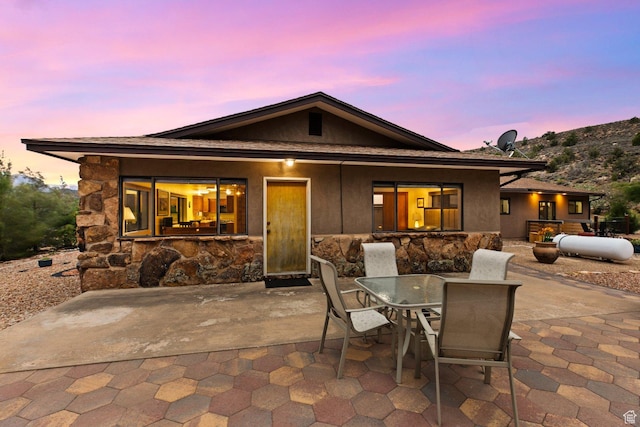 34 Valley View Dr, Springdale, UT 84767 - back of property at dusk with a patio, outdoor dining area, stone siding, and stucco siding