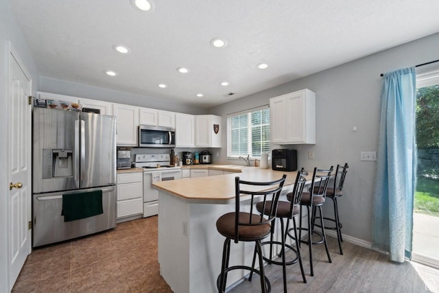 1021 Sara Ln, Ogden, UT 84404 - kitchen featuring appliances with stainless steel finishes, plenty of natural light, a peninsula, recessed lighting, and white cabinetry