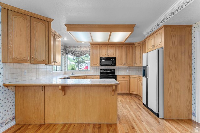 4630 S Stockbridge Ln, Millcreek, UT 84117 - kitchen with black appliances, a peninsula, light wood-style flooring, a breakfast bar area, and tasteful backsplash