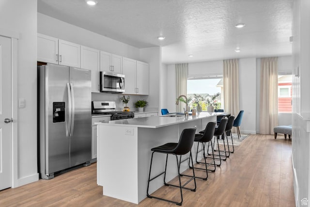 1282 N 375 E Unit 150, Harrisville, UT 84404 - kitchen featuring stainless steel appliances, a kitchen breakfast bar, a center island with sink, light wood finished floors, and white cabinetry