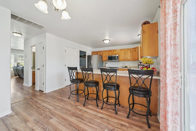 1213 E 540 N, Spanish Fork, UT 84660 - kitchen featuring appliances with stainless steel finishes, light wood finished floors, a peninsula, light countertops, and a kitchen bar