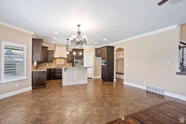 2131 S 1230 W, Syracuse, UT 84075 - kitchen featuring arched walkways, custom range hood, a center island, dark brown cabinets, and ornamental molding