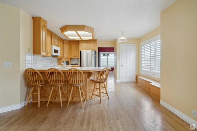 3181 E Deer Creek Cir, Cottonwood Heights, UT 84121 - kitchen with white microwave, freestanding refrigerator, tasteful backsplash, light wood finished floors, and a peninsula