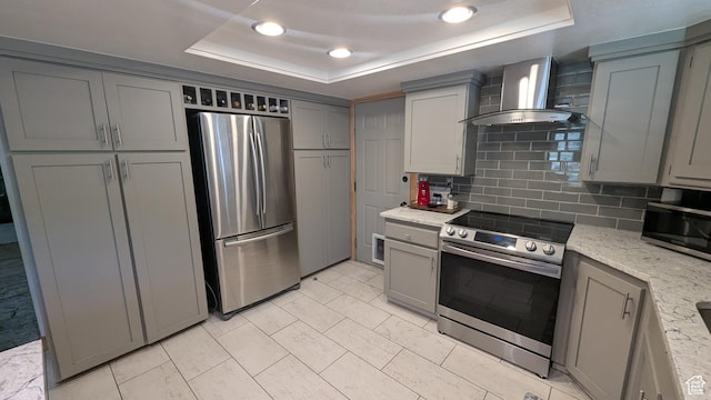 1584 E Petunia Way, Sandy, UT 84092 - kitchen featuring stainless steel appliances, wall chimney exhaust hood, gray cabinetry, a tray ceiling, and decorative backsplash