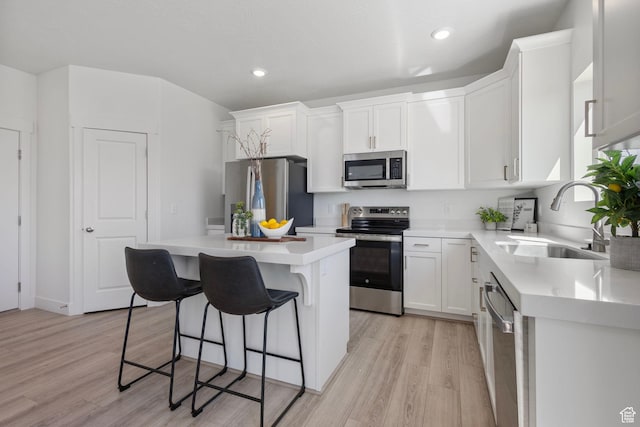 7494 N Silver Ridge Rd Unit 3466, Eagle Mountain, UT 84005 - kitchen featuring appliances with stainless steel finishes, a kitchen island, light wood finished floors, a kitchen breakfast bar, and white cabinets
