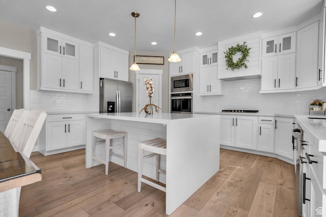 2873 S Puddle Ln, Saratoga Springs, UT 84045 - kitchen with appliances with stainless steel finishes, a kitchen bar, a kitchen island, light wood finished floors, and backsplash