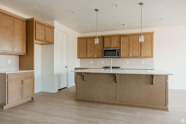 32 Rosalia Rdg, St George, UT 84770 - kitchen featuring stainless steel appliances, light wood-type flooring, backsplash, a kitchen island with sink, and brown cabinets