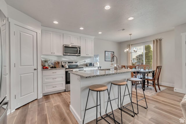 940 N Center St, Santaquin, UT 84655 - kitchen with stainless steel appliances, a chandelier, light wood-style flooring, white cabinetry, and light stone countertops