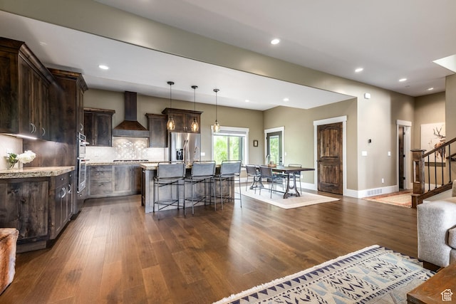 1773 E Longview Dr, Hideout, UT 84036 - kitchen featuring wall chimney range hood, stainless steel fridge with ice dispenser, dark brown cabinetry, dark wood-style flooring, and an island with sink