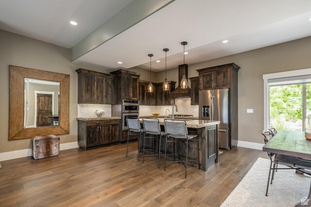1773 E Longview Dr, Hideout, UT 84036 - kitchen with stainless steel appliances, dark brown cabinets, dark wood-style floors, a kitchen breakfast bar, and decorative backsplash
