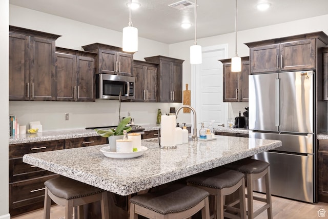 2723 S Varano Way, St George, UT 84770 - kitchen featuring stainless steel appliances, a kitchen breakfast bar, dark brown cabinets, light wood finished floors, and a kitchen island with sink