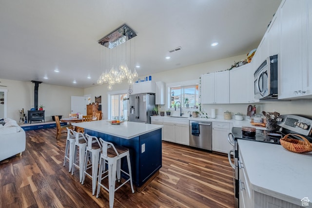 7395 N Johnson Canyon Rd, Kanab, UT 84741 - kitchen featuring appliances with stainless steel finishes, a wood stove, a center island, a kitchen bar, and dark wood-style flooring