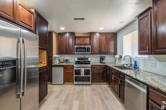 737 Carma Way, Washington, UT 84780 - kitchen featuring appliances with stainless steel finishes, light wood-style flooring, light stone counters, dark brown cabinetry, and a textured ceiling