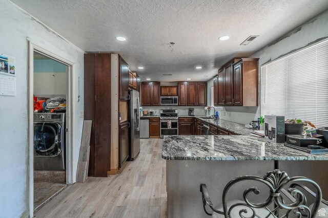 737 Carma Way, Washington, UT 84780 - kitchen with appliances with stainless steel finishes, washer / dryer, light wood-style floors, a peninsula, and light stone counters