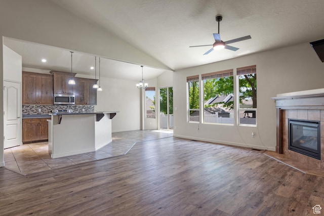 6097 W Cedar Hill Rd S, West Jordan, UT 84081 - unfurnished living room with wood finished floors, a ceiling fan, a chandelier, a tiled fireplace, and lofted ceiling