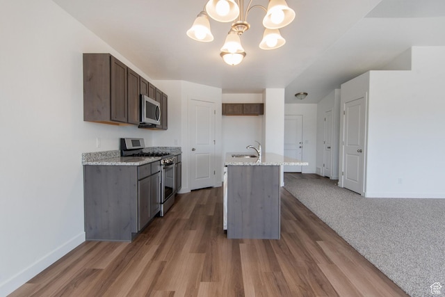 1170 W High Plains Dr Unit 609, Grantsville, UT 84029 - kitchen featuring appliances with stainless steel finishes, a chandelier, a kitchen island with sink, wood finished floors, and light stone countertops