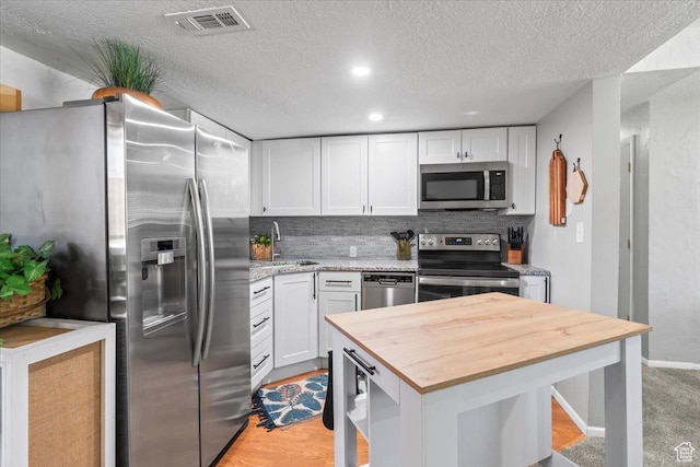 1543 E Spring Run Dr, Salt Lake City, UT 84117 - kitchen featuring stainless steel appliances, wood counters, white cabinets, a textured ceiling, and decorative backsplash