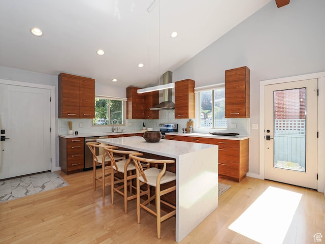 2512 E Redondo Ave S, Salt Lake City, UT 84108 - kitchen featuring stainless steel appliances, wall chimney exhaust hood, brown cabinetry, backsplash, and a kitchen breakfast bar