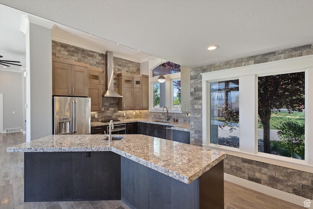 11989 S 3600 W, Riverton, UT 84065 - kitchen with high end refrigerator, wall chimney exhaust hood, crown molding, light stone counters, and an island with sink