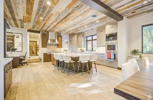 4896 Last Stand Dr, Snyderville, UT 84098 - kitchen with wall chimney range hood, appliances with stainless steel finishes, a large island, a kitchen breakfast bar, and light countertops