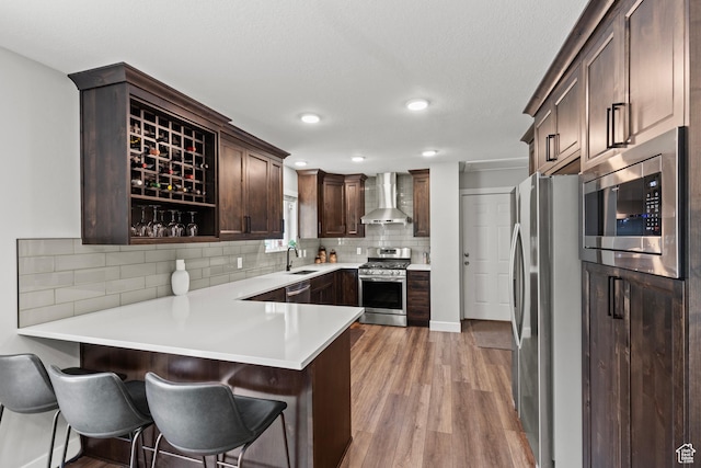 332 E 2475 N, North Logan, UT 84341 - kitchen featuring stainless steel appliances, wall chimney range hood, light wood-style floors, a peninsula, and dark brown cabinets