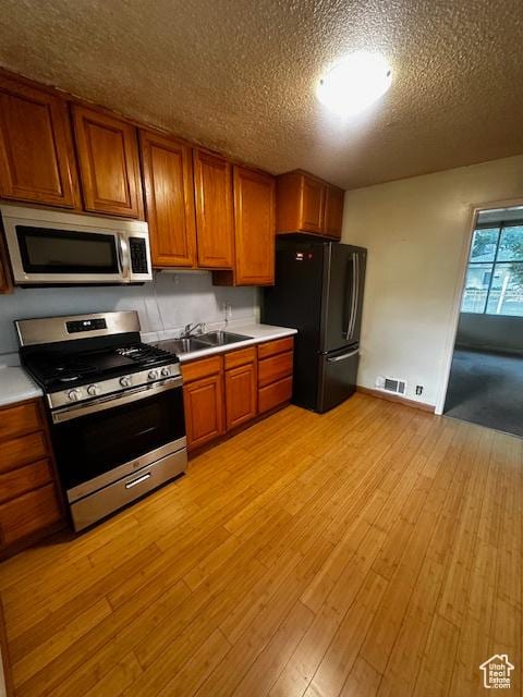 3700 S 3325 W, West Valley City, UT 84119 - kitchen featuring stainless steel appliances, brown cabinets, light countertops, light wood-style floors, and a textured ceiling