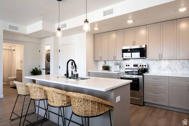 875 W Akoya Pearl St Unit 205, St George, UT 84790 - kitchen with stainless steel appliances, stacked washer / dryer, gray cabinetry, light countertops, and a center island with sink