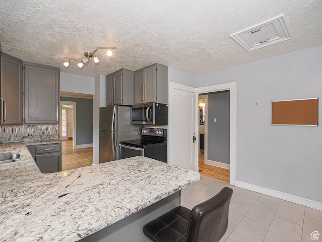 1527 E Princeton Ave S, Salt Lake City, UT 84105 - kitchen featuring appliances with stainless steel finishes, a breakfast bar area, light stone counters, a peninsula, and a textured ceiling