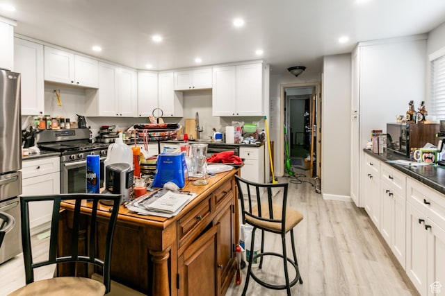 5841 S Fontaine Bleu Dr E, Murray, UT 84121 - kitchen with a center island, dark countertops, stainless steel appliances, light wood finished floors, and white cabinetry