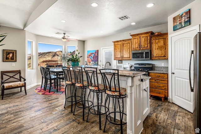 93 E 700 N, La Verkin, UT 84745 - kitchen featuring stainless steel appliances, brown cabinets, dark wood-style floors, a kitchen island with sink, and a kitchen bar