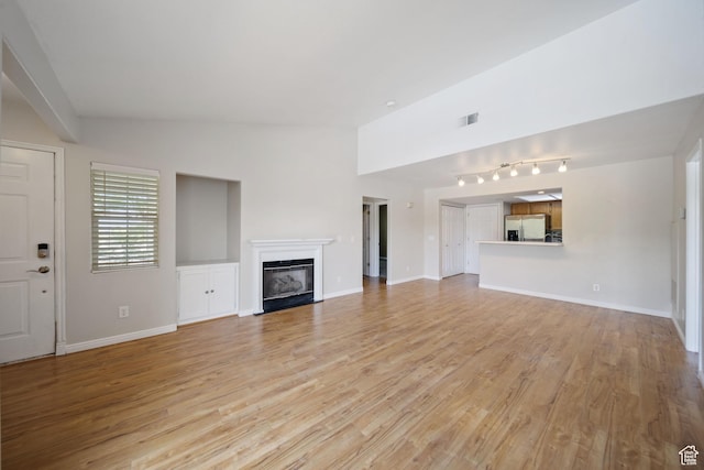 3807 S River Run Way Unit 3, Salt Lake City, UT 84119 - unfurnished living room with a glass covered fireplace, light wood-type flooring, rail lighting, and vaulted ceiling