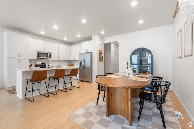 938 W Terracotta Dr, Saratoga Springs, UT 84045 - kitchen featuring stainless steel appliances, a kitchen bar, a kitchen island with sink, light wood finished floors, and white cabinetry