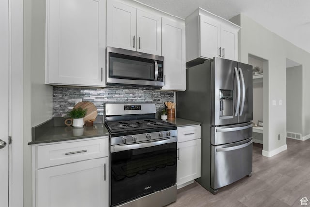 1666 W Rockaway Ln, West Jordan, UT 84084 - kitchen featuring stainless steel appliances, decorative backsplash, light wood-type flooring, white cabinets, and dark countertops