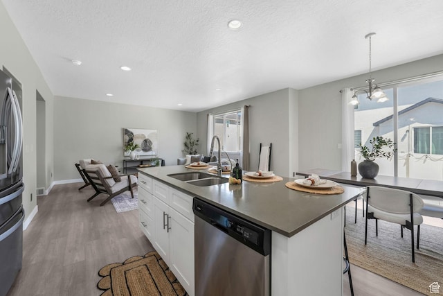1666 W Rockaway Ln, West Jordan, UT 84084 - kitchen with appliances with stainless steel finishes, wood finished floors, white cabinets, a center island with sink, and decorative light fixtures