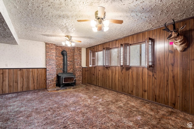 5374 S 5700 W, Hooper, UT 84315 - unfurnished living room with wooden walls, a wood stove, ceiling fan, a textured ceiling, and carpet flooring