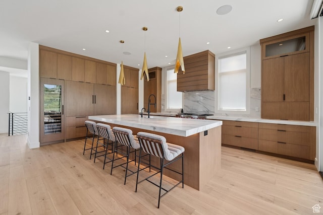 1404 W Ursa Way, Heber City, UT 84032 - kitchen with wall chimney exhaust hood, light wood-style floors, a breakfast bar area, a large island with sink, and recessed lighting