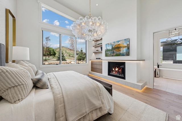 1404 W Ursa Way, Heber City, UT 84032 - bedroom featuring wood finished floors, a towering ceiling, multiple windows, a chandelier, and a glass covered fireplace